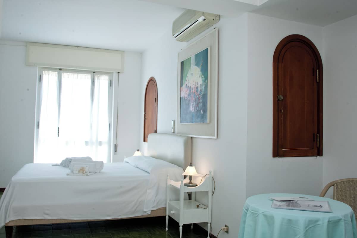 Ein Hotelzimmer mit einem Bett, einem Nachttisch mit Lampe, einem kleinen Tisch mit einer Zeitschrift und einem Bild an der Wand.