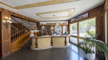 Una hall con una scala in legno, una reception e un'ampia finestra con vista su palme.
