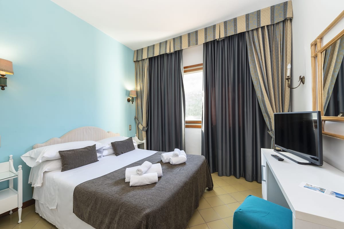 Ein Hotelzimmer mit Bett, Schreibtisch, Fernseher und einem Fenster mit Vorhängen.