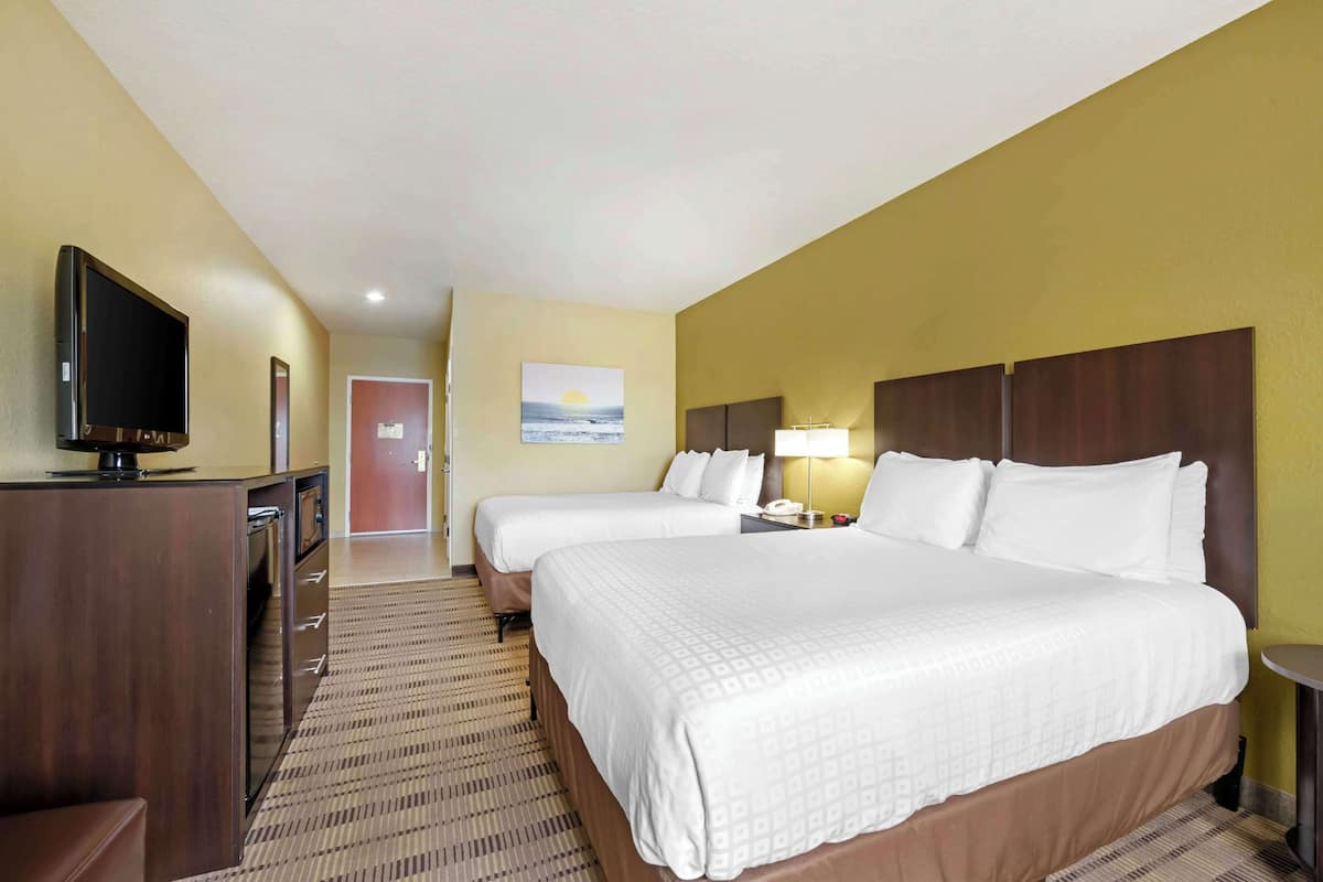 A hotel room with two beds, a TV, a desk, and a painting on the wall.