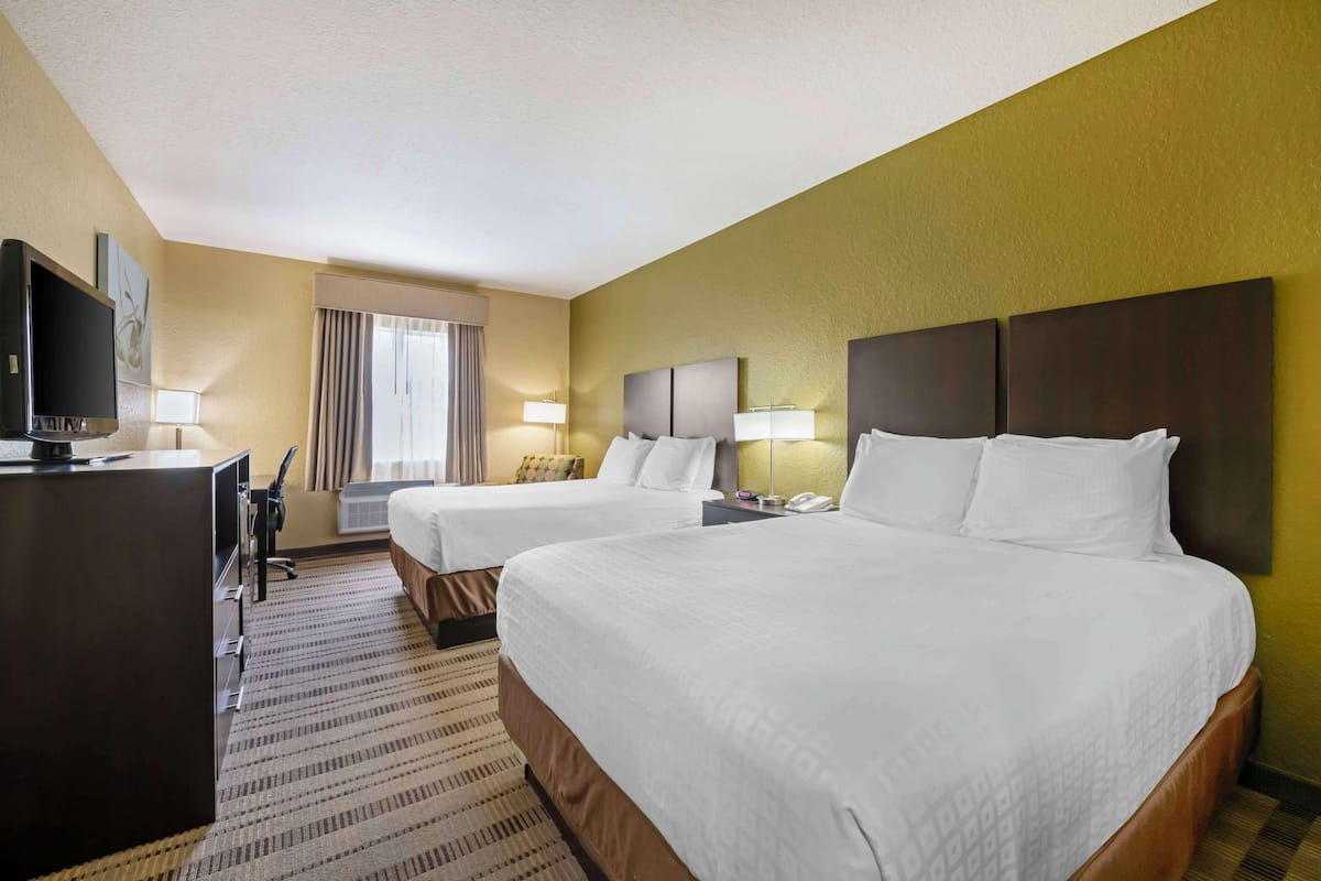 A hotel room with two beds, a desk with a TV, and a window with curtains.