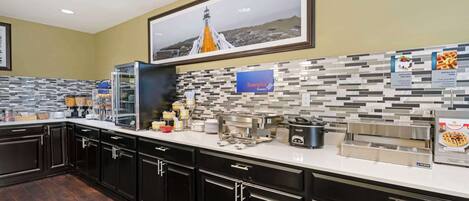 A modern kitchen with black cabinets, a white countertop, and a tiled backsplash. There are various kitchen appliances and a framed picture on the wall.