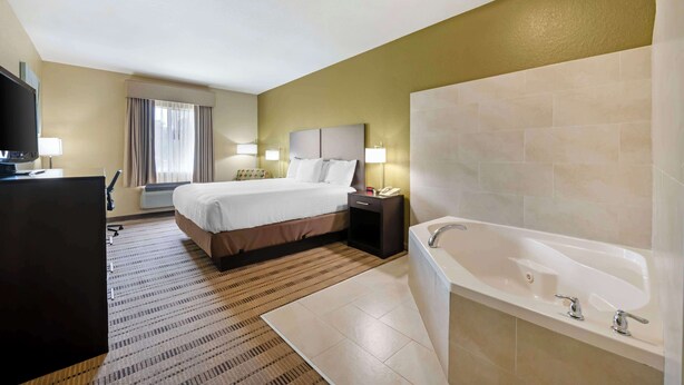 Een hotelkamer met een bed, nachtkastje, lamp en een groot bad.
