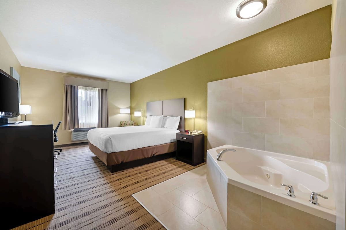 A hotel room with a bed, bedside table, lamp, and a large bathtub.