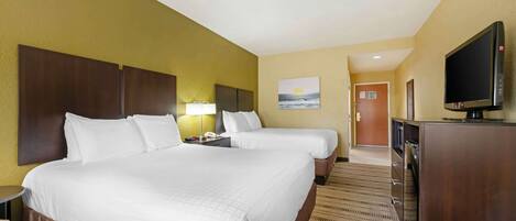 A hotel room with two beds, a television, a desk with a lamp, and a painting of a sunset.