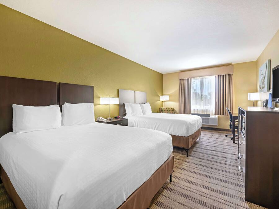 Ein Hotelzimmer mit zwei Betten, einem Schreibtisch, einem Fernseher und einem Fenster mit Vorhängen.