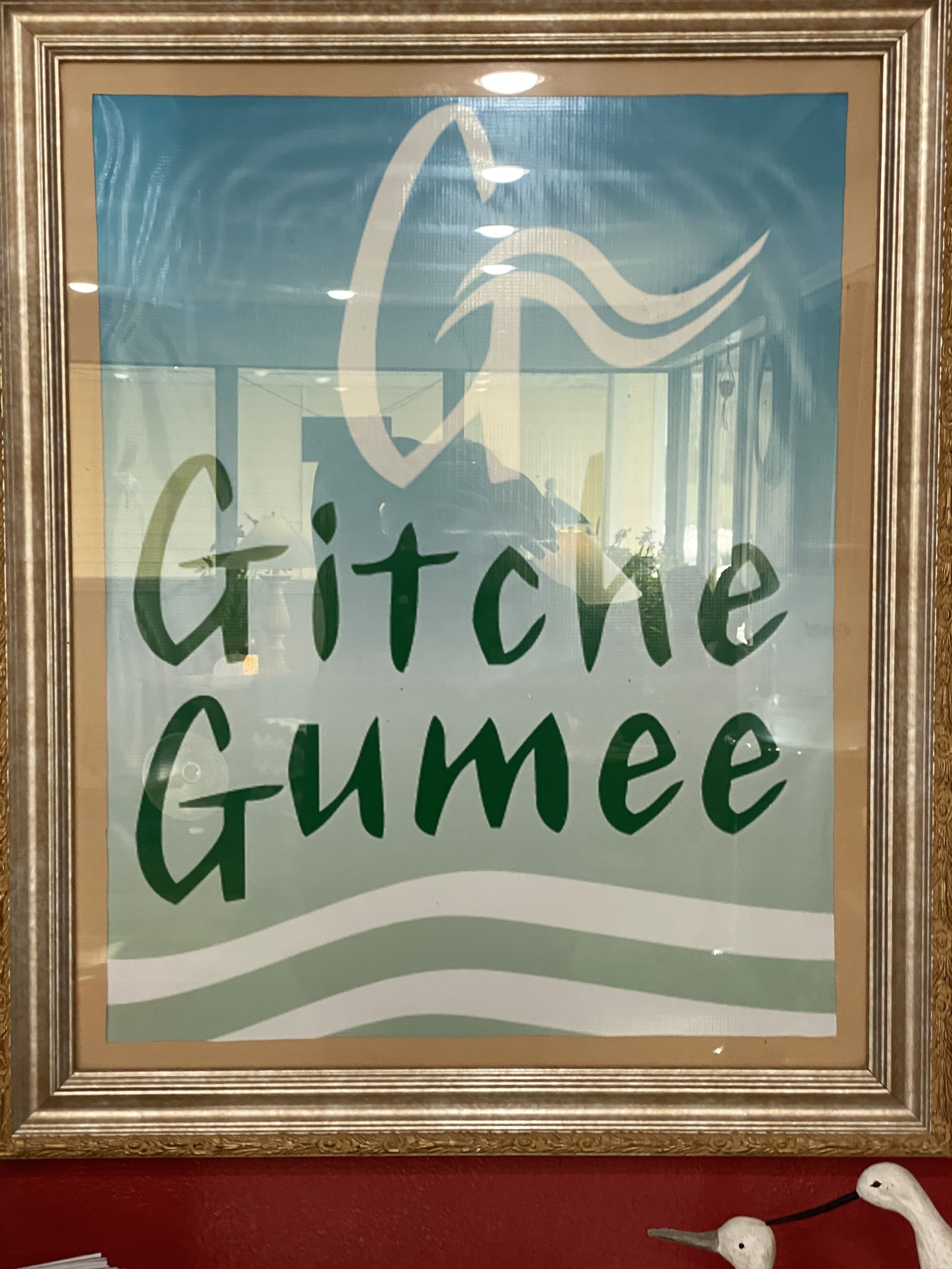 Une plaque encadrée portant l’inscription « Gitche Gumee » et un motif stylisé d’oiseau.