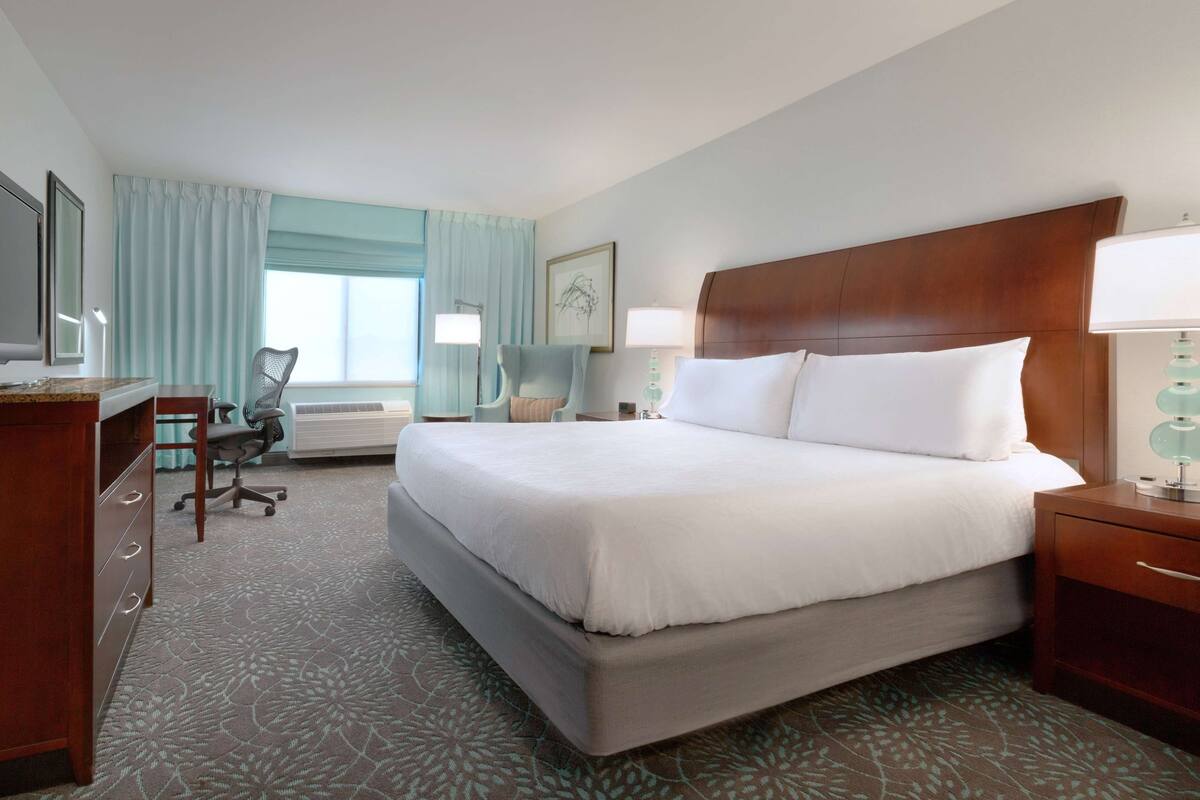 A hotel room with a large bed, a desk, a chair, and a TV.