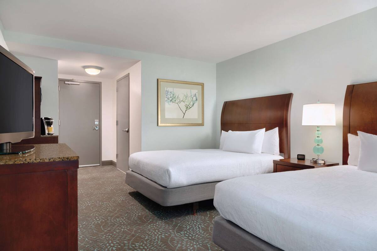 A hotel room with two beds, a television, a framed artwork on the wall, and a patterned carpet.