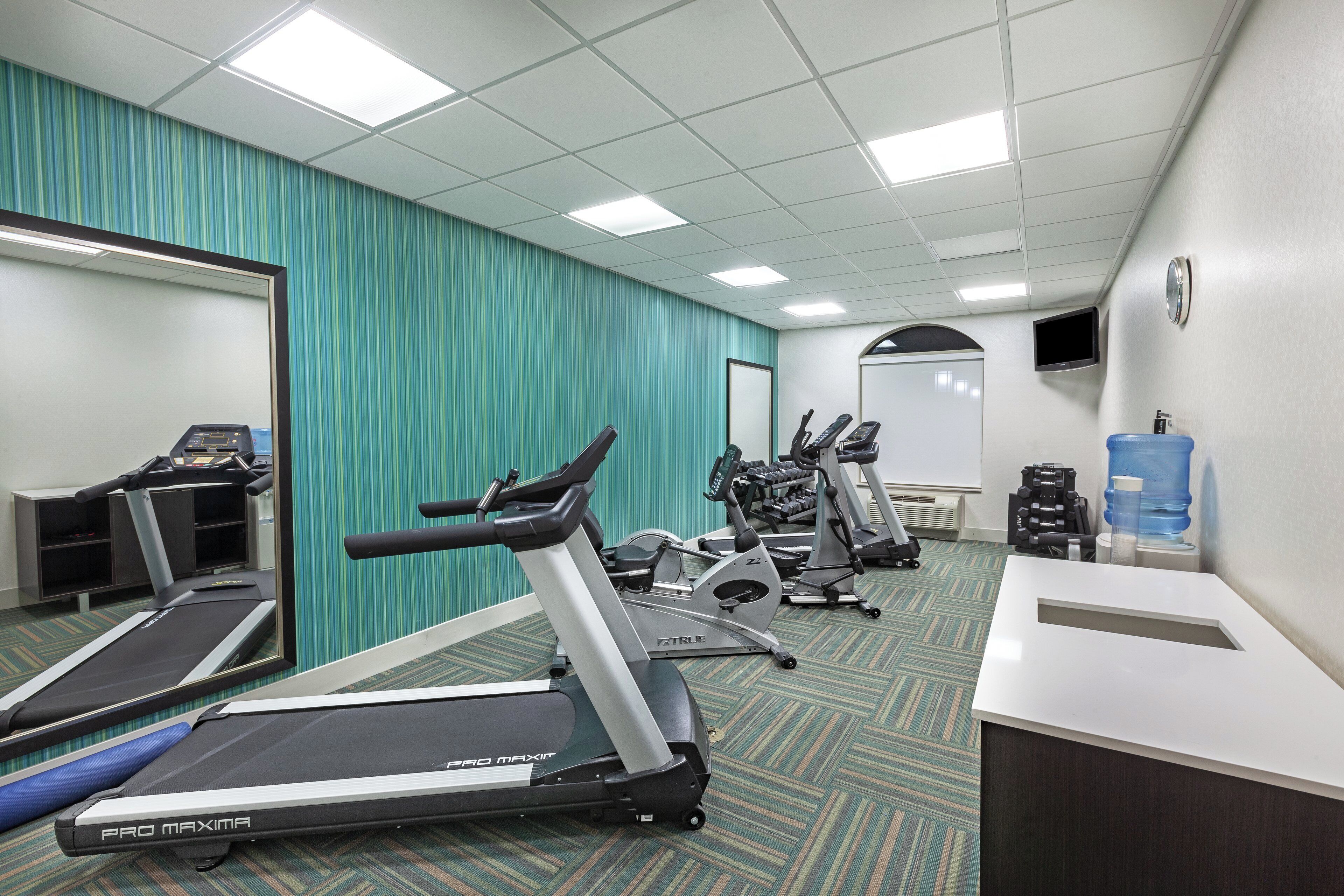 A fitness room with treadmills, exercise bikes, and dumbbells.