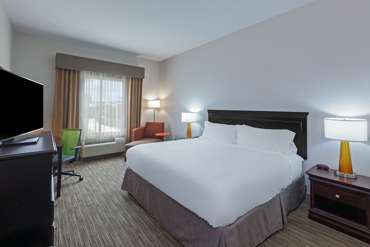 Une chambre d’hôtel avec un grand lit, un bureau doté d’un téléviseur à écran plat, une chaise, une lampe et une table de chevet.