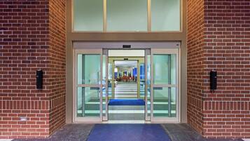 A building entrance with glass doors, a blue mat, and a brick wall.