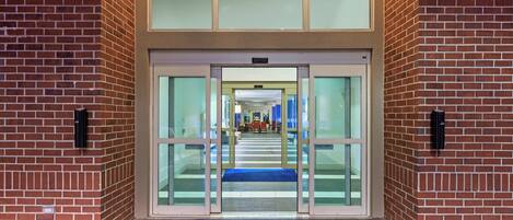 A building entrance with glass doors, a blue mat, and a brick wall.
