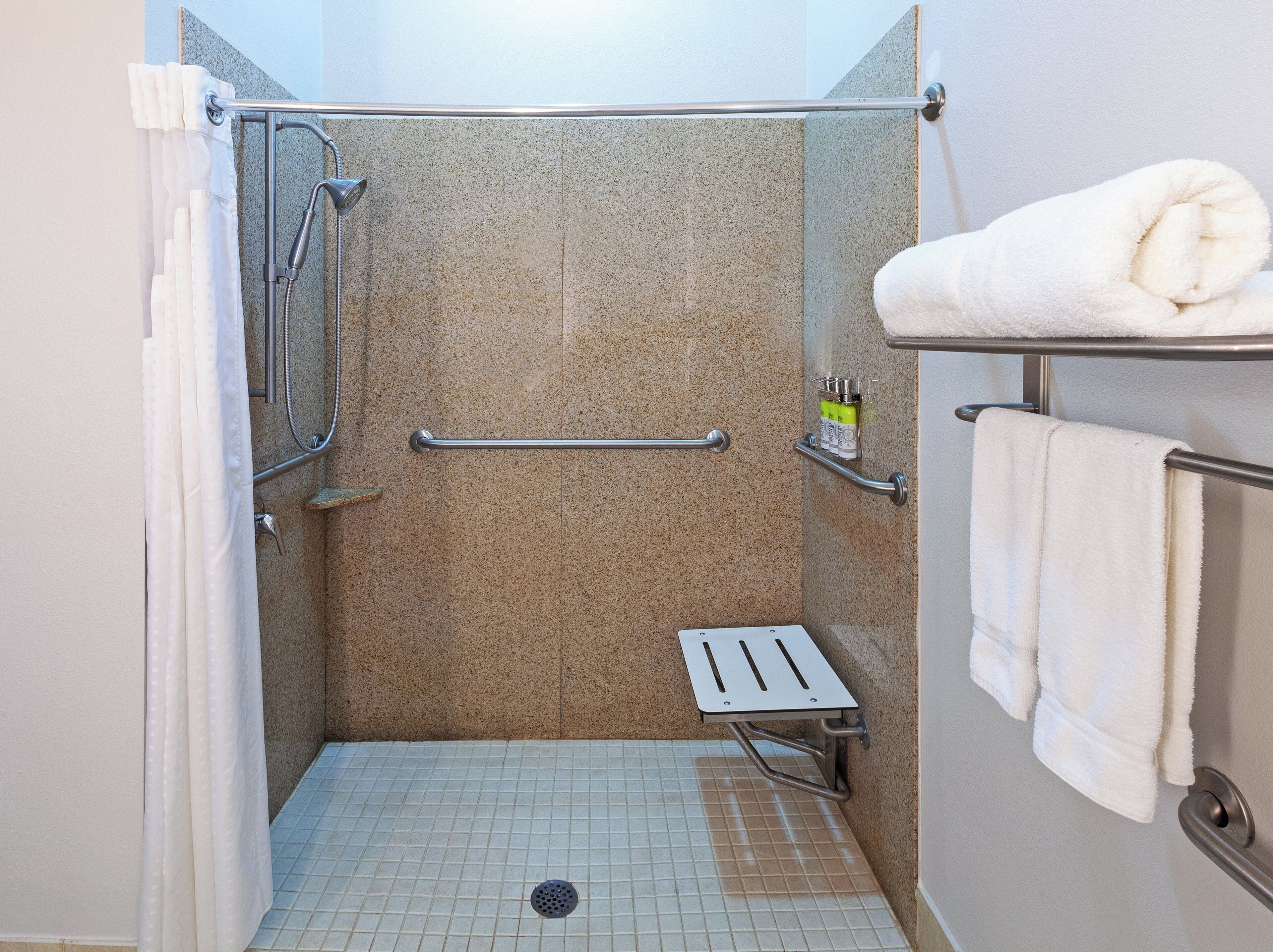 A shower area with a grab bar, a towel rack, and a shelf with toiletries.