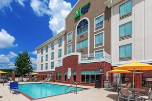 A Holiday Inn Express building with a swimming pool, outdoor seating, and a clear blue sky. - Holiday Inn Express & Suites Shreveport South Park Plaza by IHG (Shreveport)