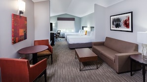 Quarto de hotel com uma cama, dois sofás, uma mesa de jantar e uma televisão.