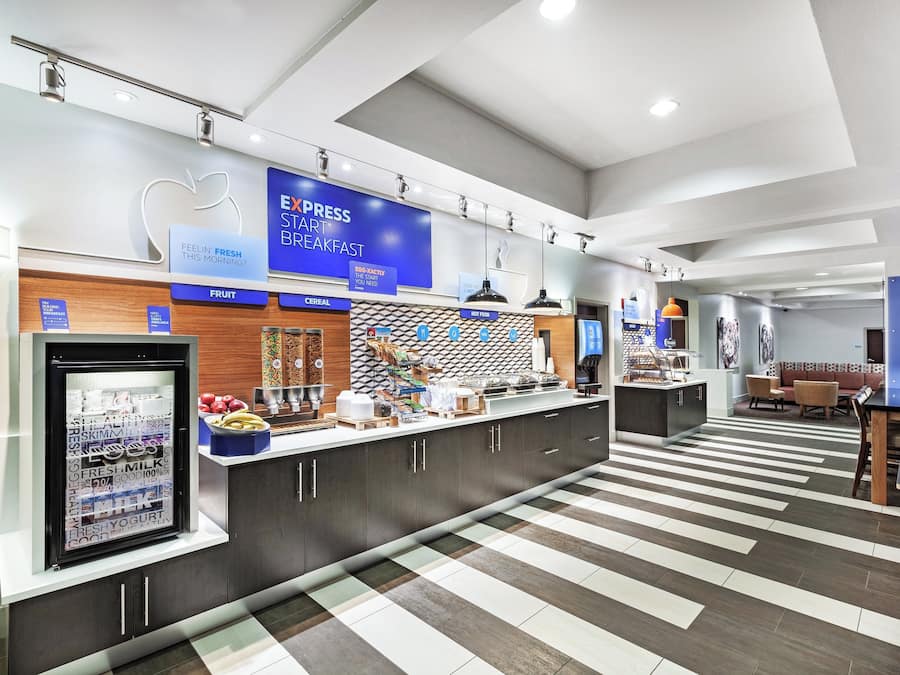 A breakfast area with a self-serve station, refrigerated display, and various food options.