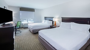 Quarto de hotel com duas camas, uma escrivaninha com televisão, uma cadeira e uma janela com vista.