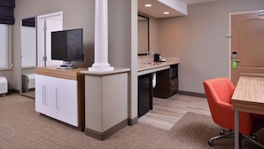 Una habitación de hotel con kitchenette, televisión, escritorio y silla.