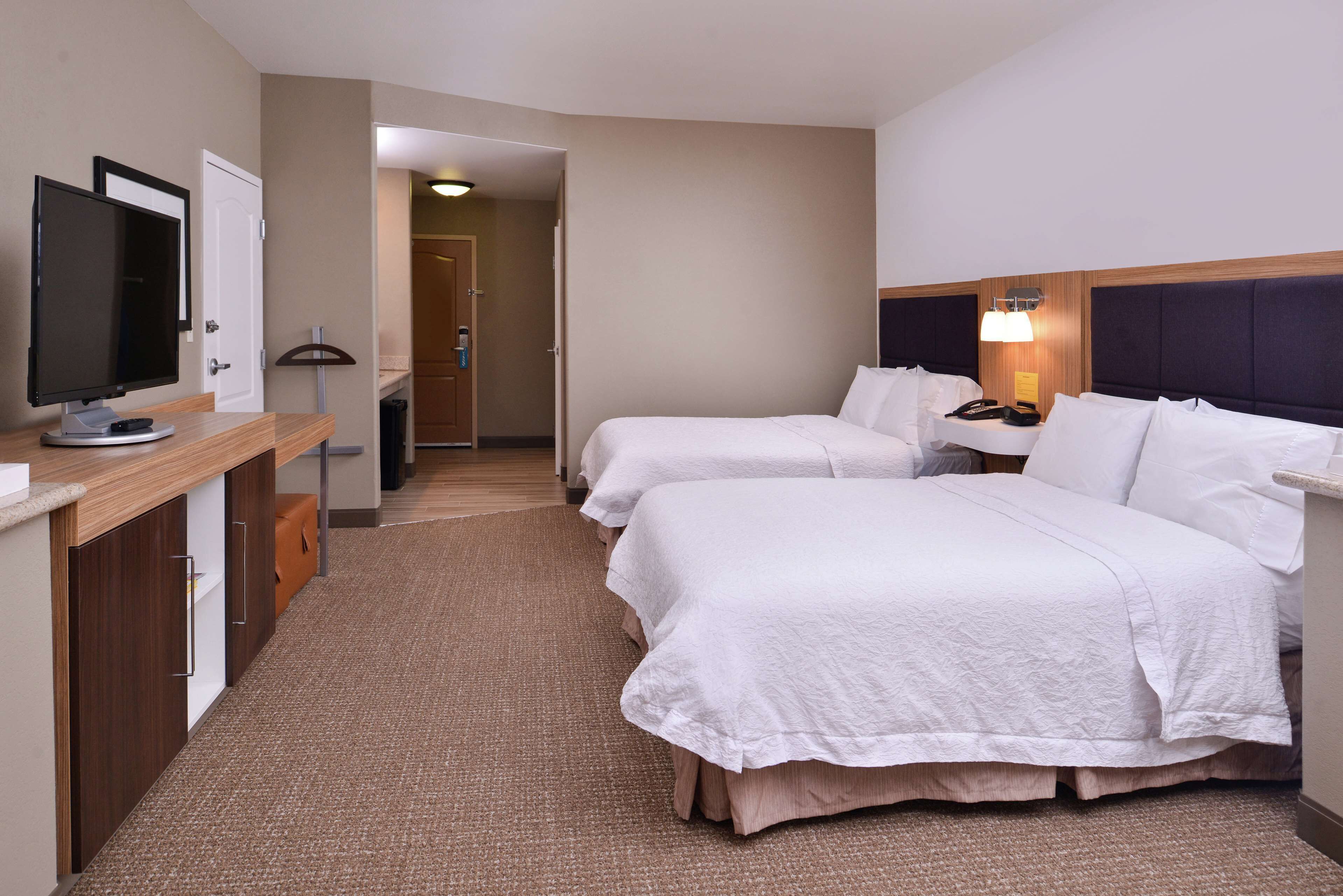 Ein Hotelzimmer mit zwei Betten, einem Schreibtisch mit Computer, einem Fernseher und einer Lampe.