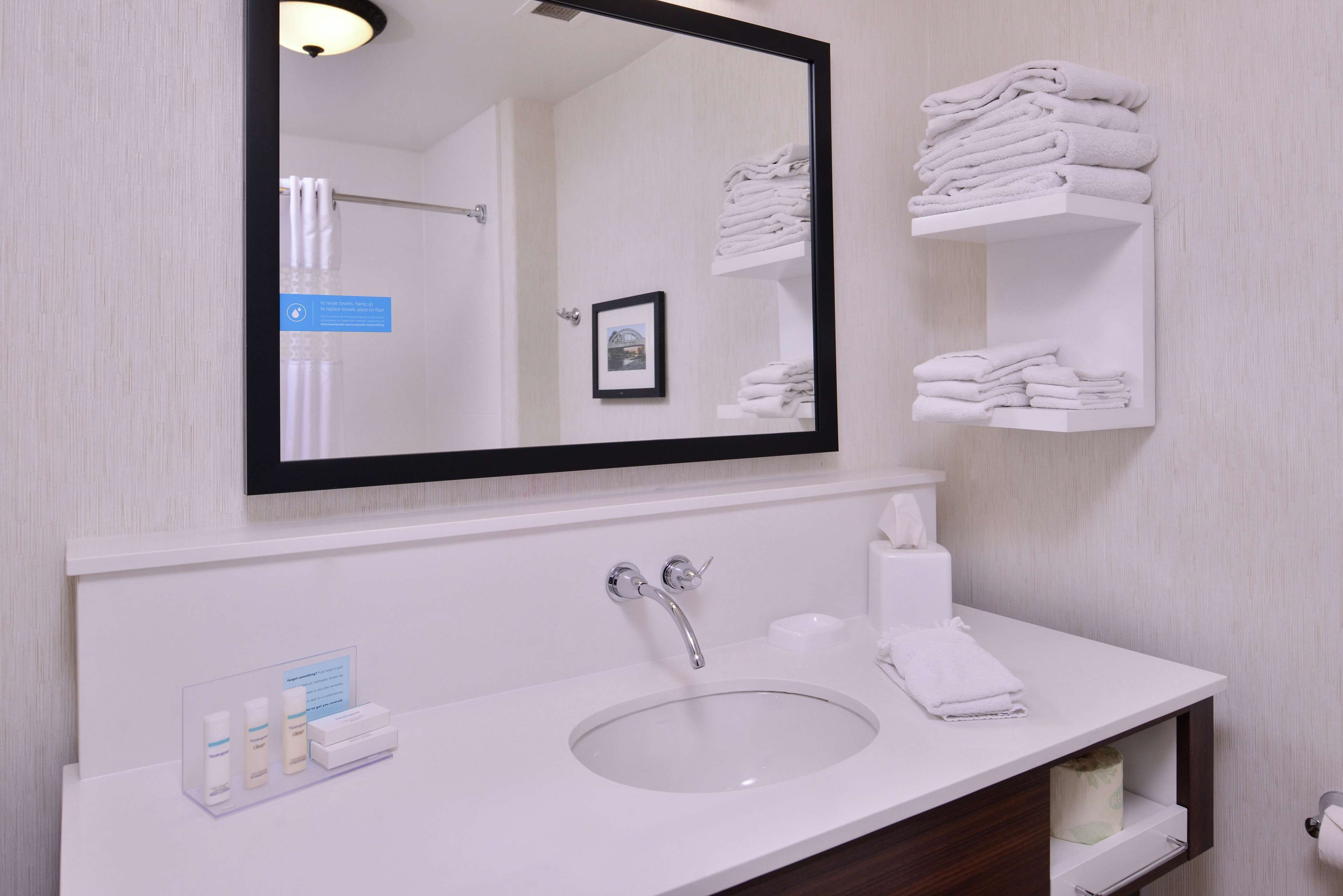 Un baño con lavamanos blanco, un espejo y estantes con toallas dobladas.