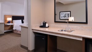 Una habitación de hotel con una cama, una mesita de noche, un escritorio, un lavabo y un espejo.