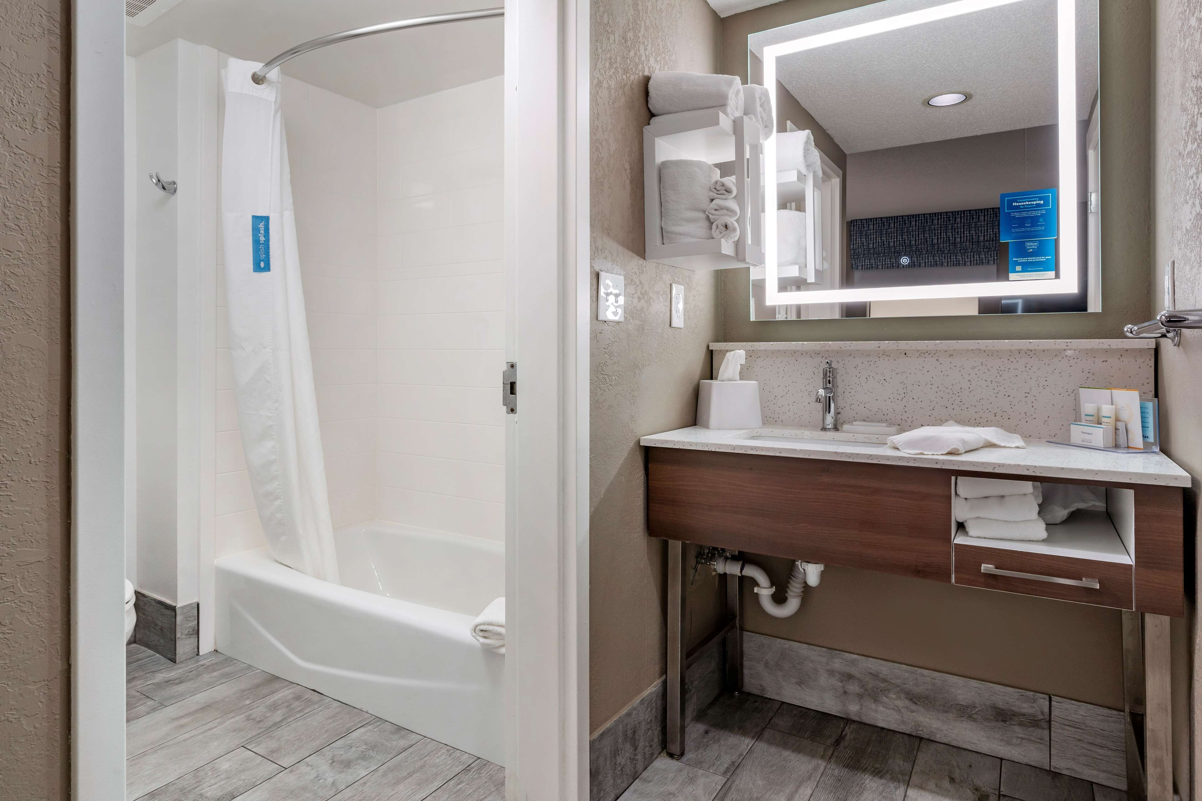 A modern bathroom with a white bathtub, a vanity with a mirror, and a towel rack.