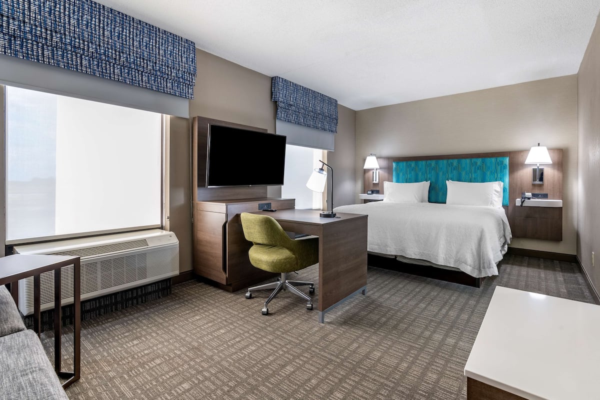 A hotel room with a bed, a desk with a chair, a television, and a window.