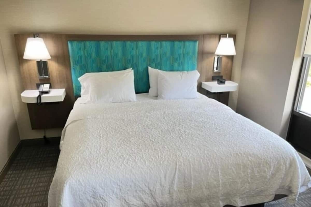 A hotel room with a large bed, two bedside tables with lamps, a teal-colored headboard, and a window.