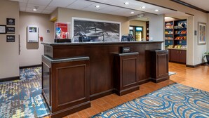 A hotel reception desk with a digital kiosk, a large poster, and a snack bar in the background. - Hampton Inn & Suites Louisville East (Louisville)