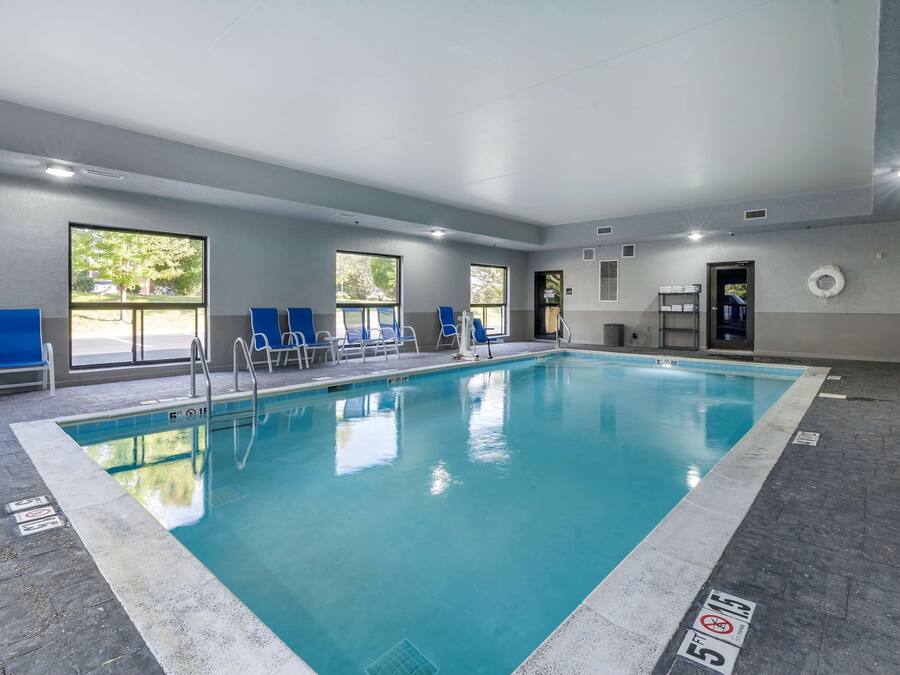 Ein beheiztes Hallenbad mit klarem, blauem Wasser, umgeben von blauen Stühlen und großen Fenstern, die für natürliches Licht sorgen.