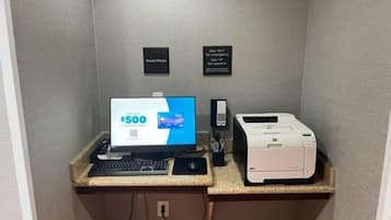 Un escritorio pequeño con un monitor de computadora mostrando una oferta de “$500”, una impresora y un teclado.