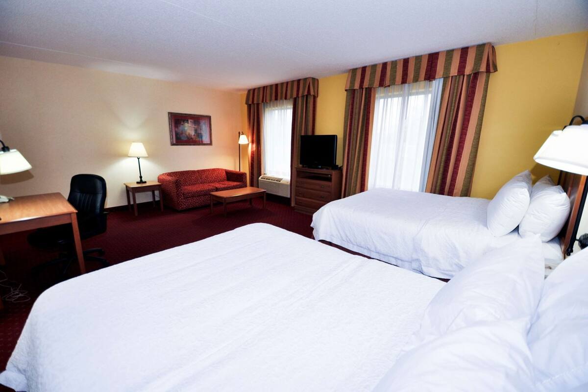 Habitación de hotel con dos camas, un escritorio, una silla, un televisor y una lámpara.