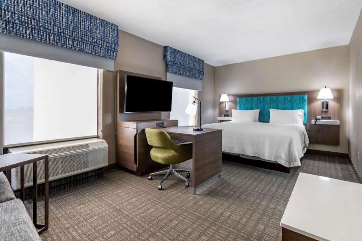 A hotel room with a bed, desk, chair, TV, and two bedside lamps.