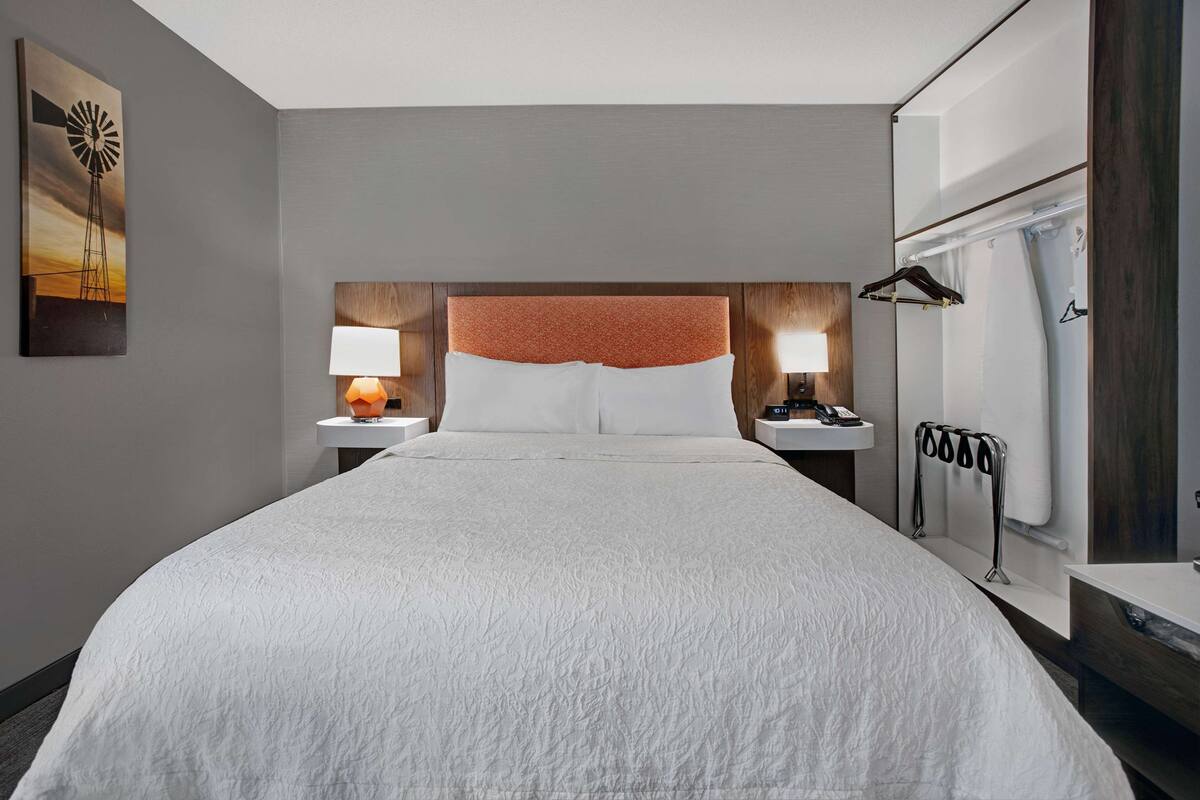 A hotel room with a large bed, two bedside tables with lamps, a wooden headboard, a mirror, and a shower curtain.