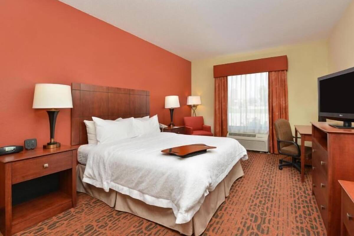 A hotel room with a bed, bedside tables, lamps, a TV, a desk, and a chair.