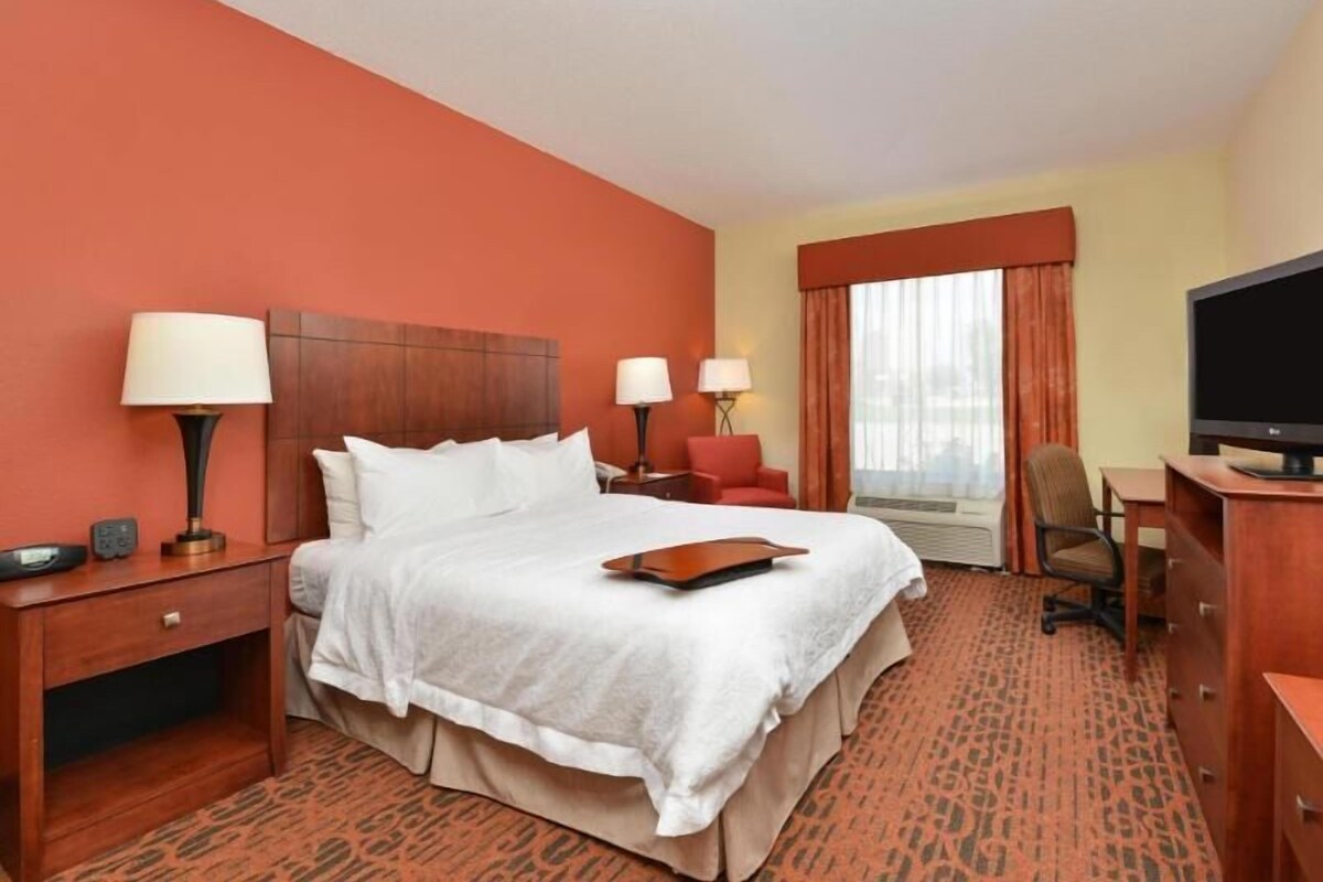 A hotel room with a bed, bedside tables, lamps, a TV, a desk, and a chair.
