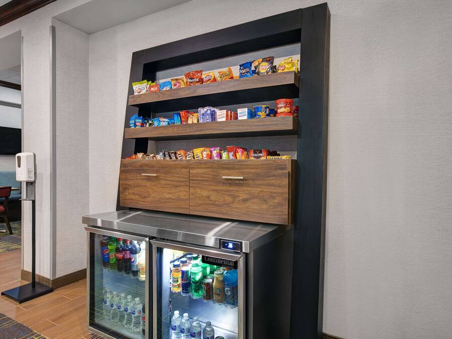 A hotel room with a minibar, a refrigerator stocked with beverages, and a shelf with snacks.
