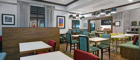 A modern restaurant with wooden tables and chairs, a bar area, and framed artwork on the walls.