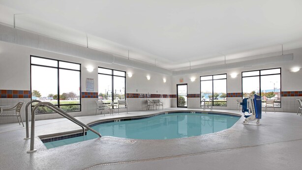 A large indoor swimming pool with a lifeguard chair, poolside chairs, and a view of the outside through large windows. - Hampton Inn Keokuk (Keokuk)