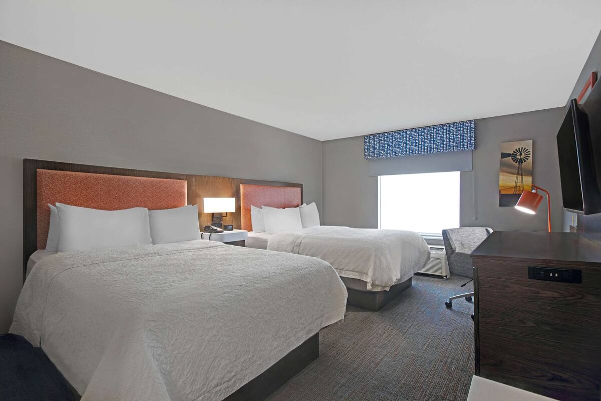 A hotel room with two beds, a desk, a chair, a TV, and a window with a view.