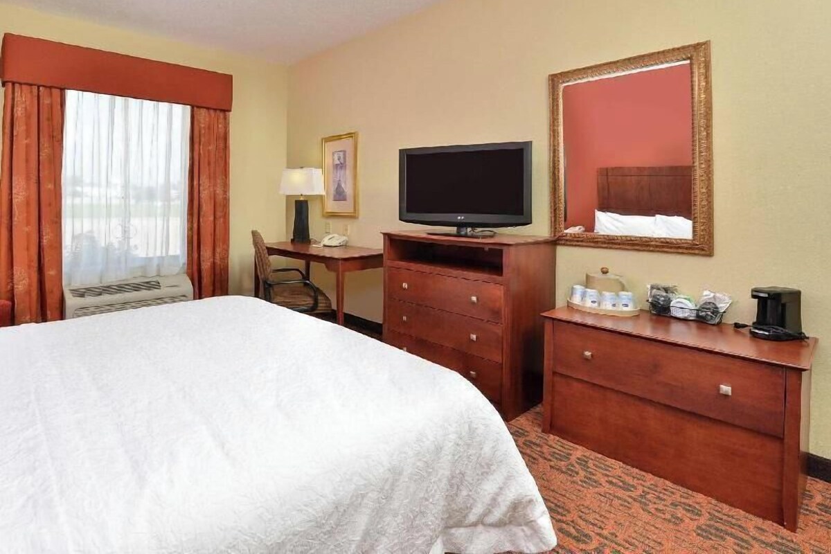 A hotel room with a bed, a desk with a television, a dresser, and a mirror.