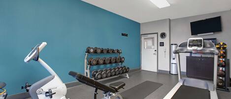 A gym with exercise equipment, a wall-mounted TV, and a rack of dumbbells.