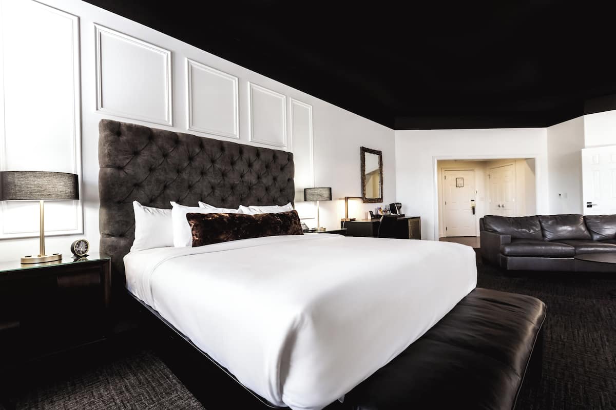 A hotel room with a large bed, a dark leather sofa, a desk, and a mirror.
