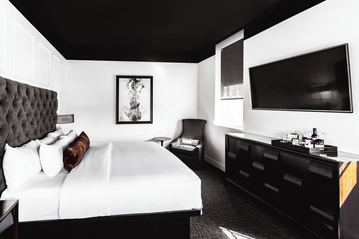 A modern hotel room with a large bed, a flat-screen TV, a small side table, and a dark-toned wardrobe.