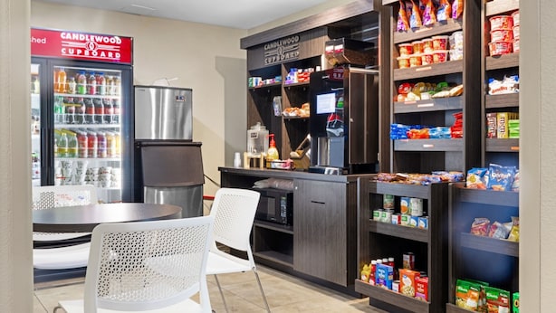 A kitchenette with a refrigerator, microwave, and coffee machine, and shelves stocked with snacks and beverages.