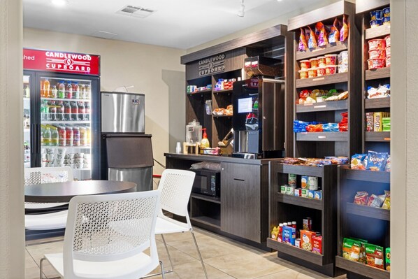 A kitchenette with a refrigerator, microwave, and coffee machine, and shelves stocked with snacks and beverages.