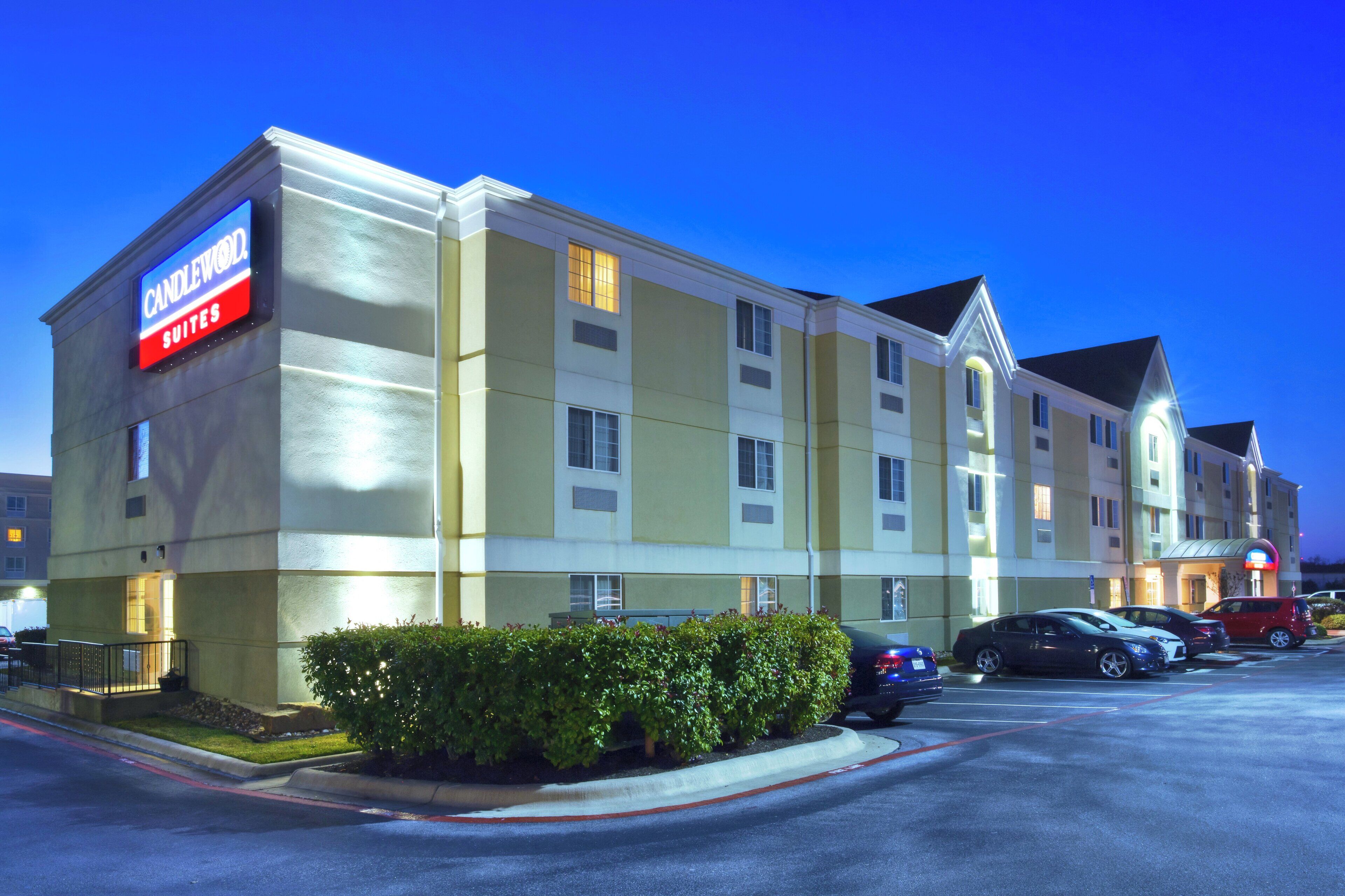 Un hotel con un letrero que dice 'CANDLEWOOD SUITES' y un estacionamiento con varios coches.