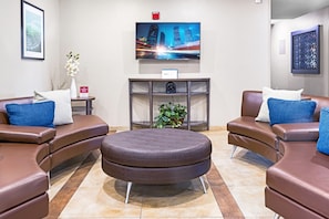 A lobby with leather sofas, a round ottoman, a TV, a plant, and a framed picture on the wall. - Candlewood Suites Killeen - Fort Hood Area by IHG (Killeen)