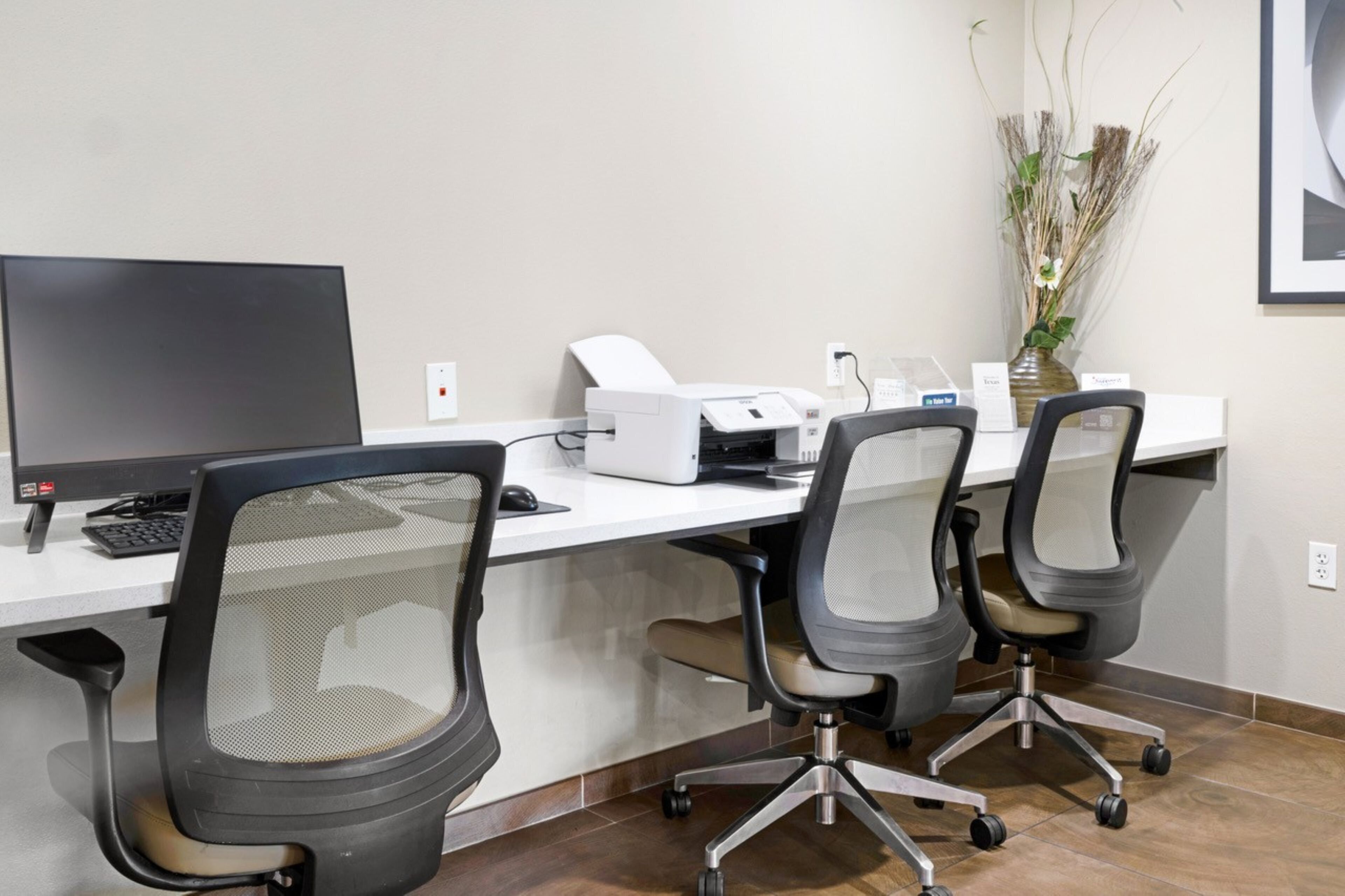 Un bureau moderne équipé d’un bureau, d’un ordinateur, d’une imprimante et de chaises de bureau.